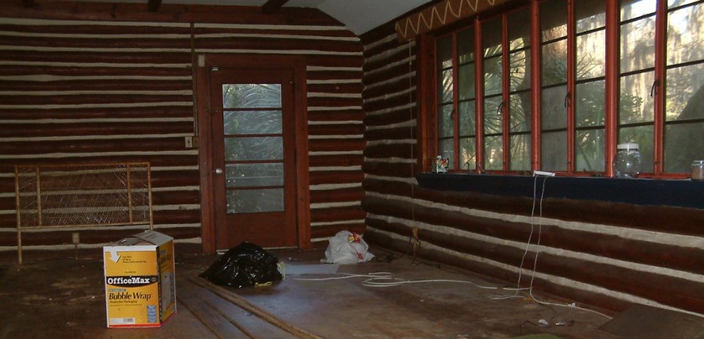 Inside a log cabin build. This is a picture of our living room after we had left. It is showing the logs and cement filling painted white. Shows the old-fashioned solid, hand turning Florida windows, wooden floors and visible hand-hewn logs/braces on ceiling.